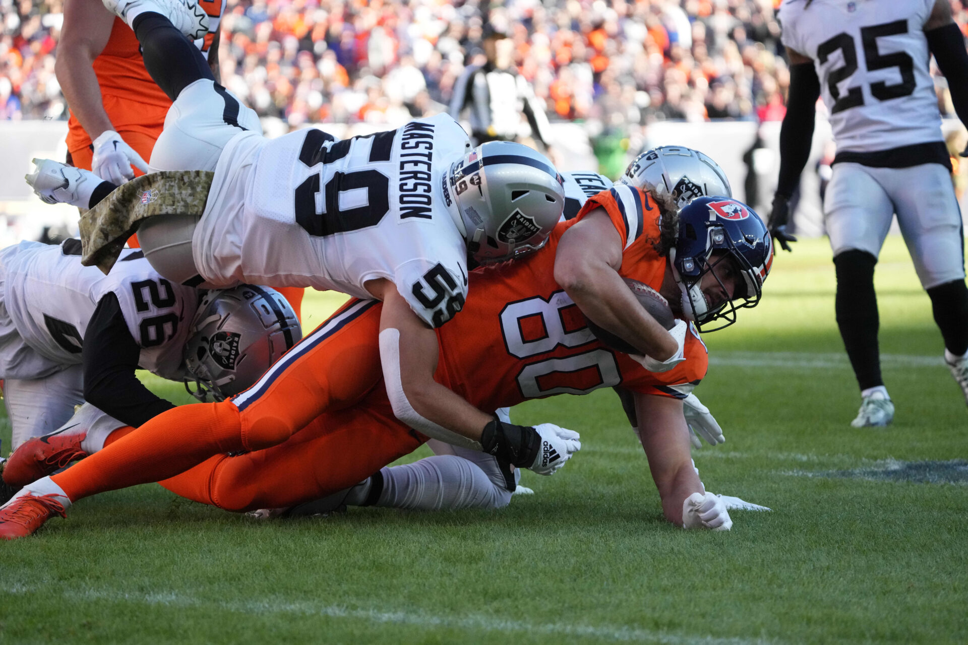 Denver Broncos tight end Greg Dulcich, in an orange uniform, is tackled and taken to the ground by several Las Vegas Raiders.