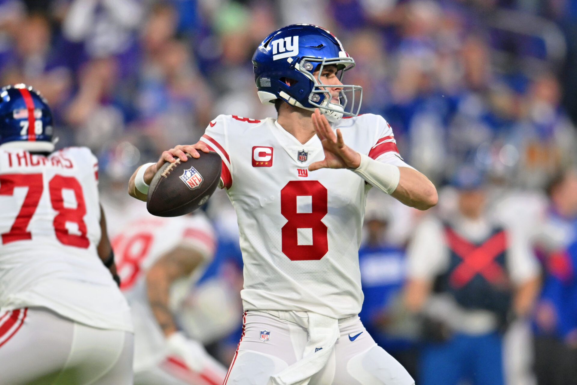 New York Giants quarterback Daniel Jones (in a white jersey with red accents, white pants a blue helmet) drops back to throw a pass