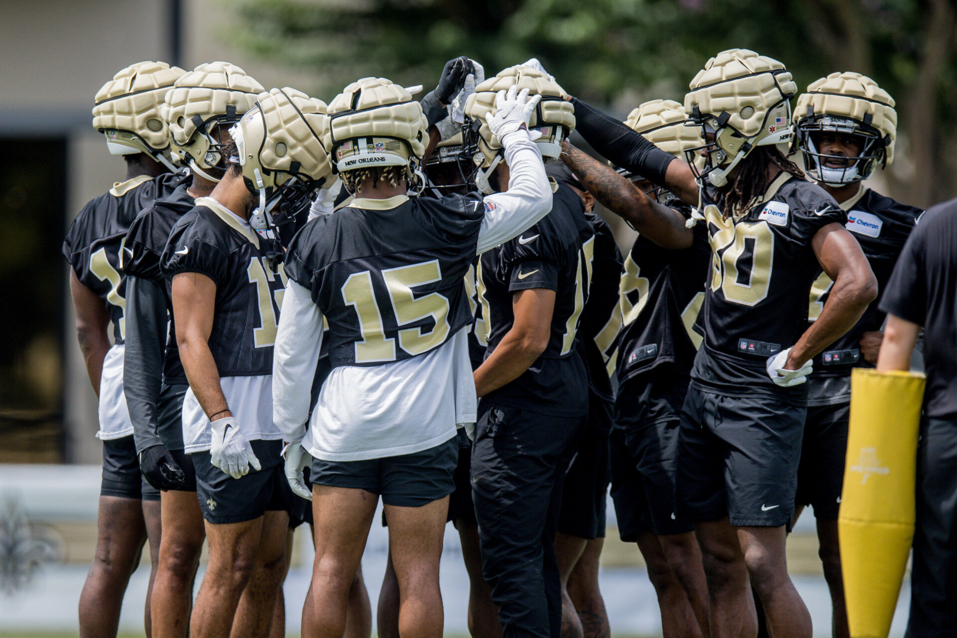 New Orleans Saints players in practice jersey huddled with their hands on a single player's helmet