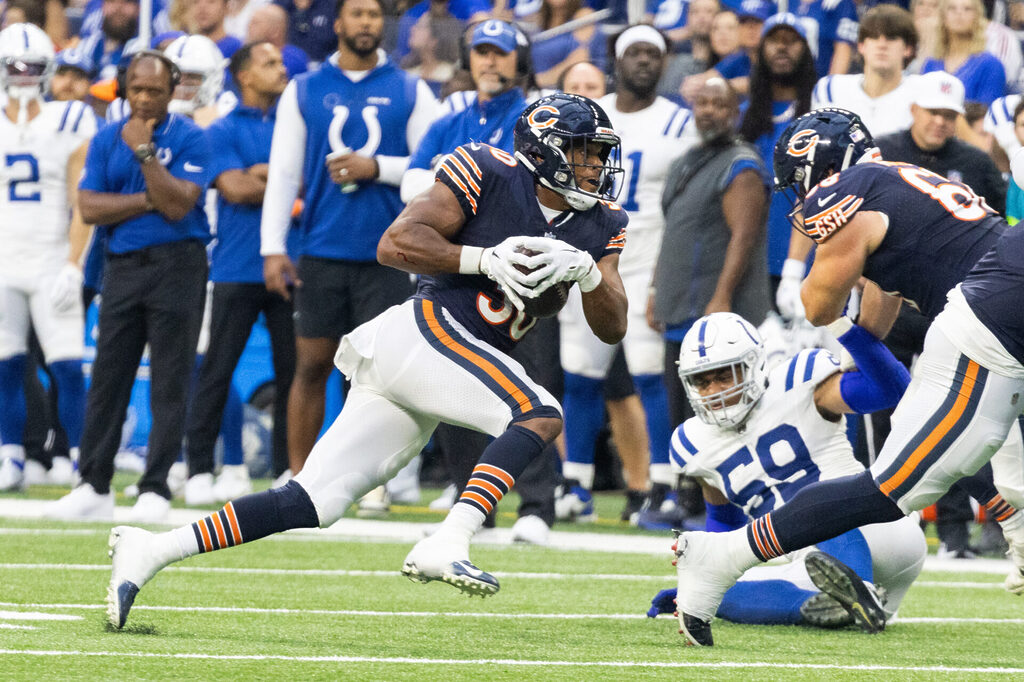 Roschon Johnson, in a dark blue jersey and helmet and white pants, runs past a Chicago teammate and a Colts defender on the ground