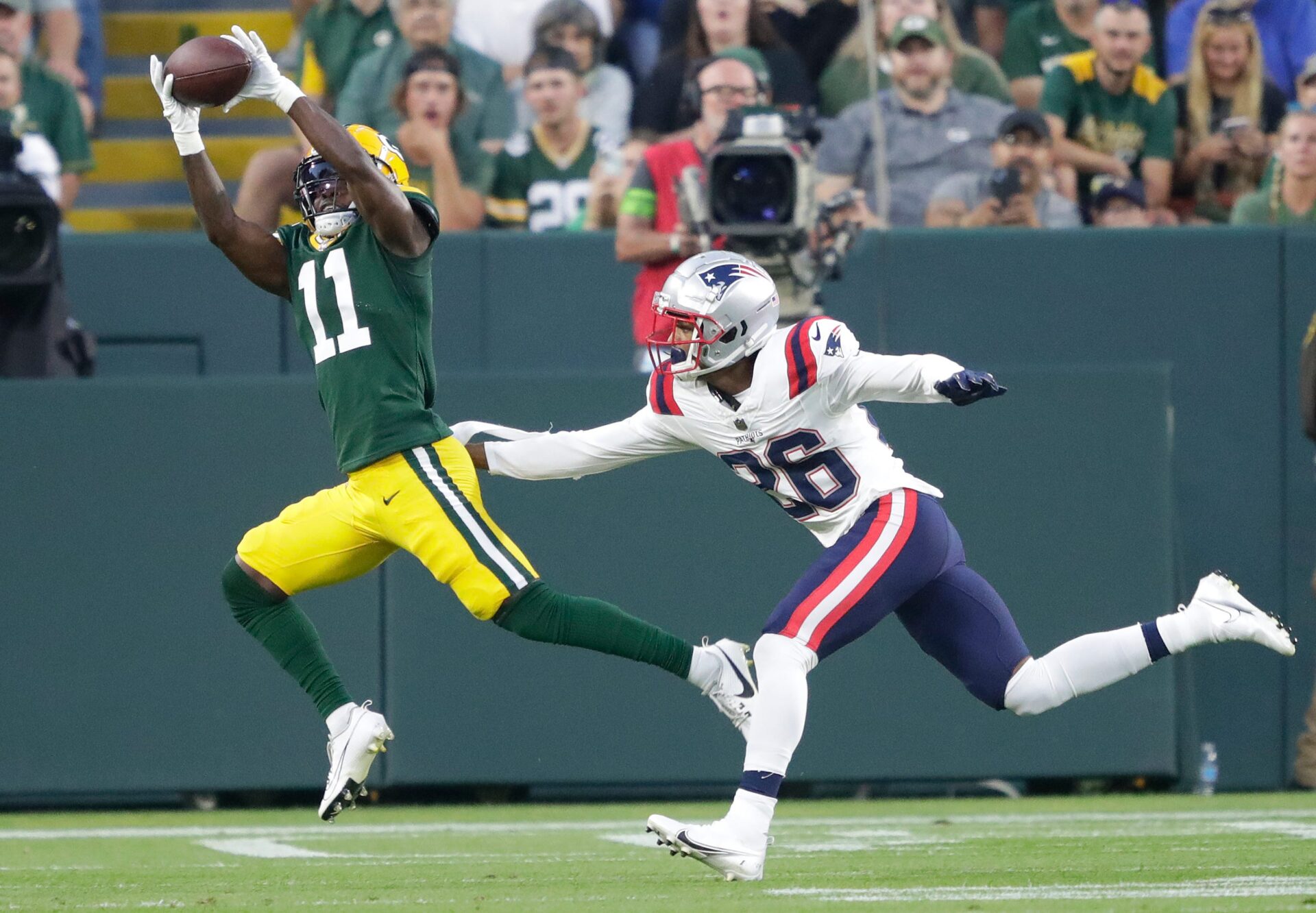 Jayden Reed makes a leaping catch as a Patriots player trails behind him and grabs Reed's pants