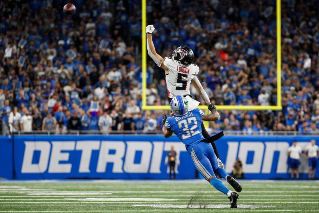 Drake London leaps in the air while Brian Branch has his arms near him while the ball sails away