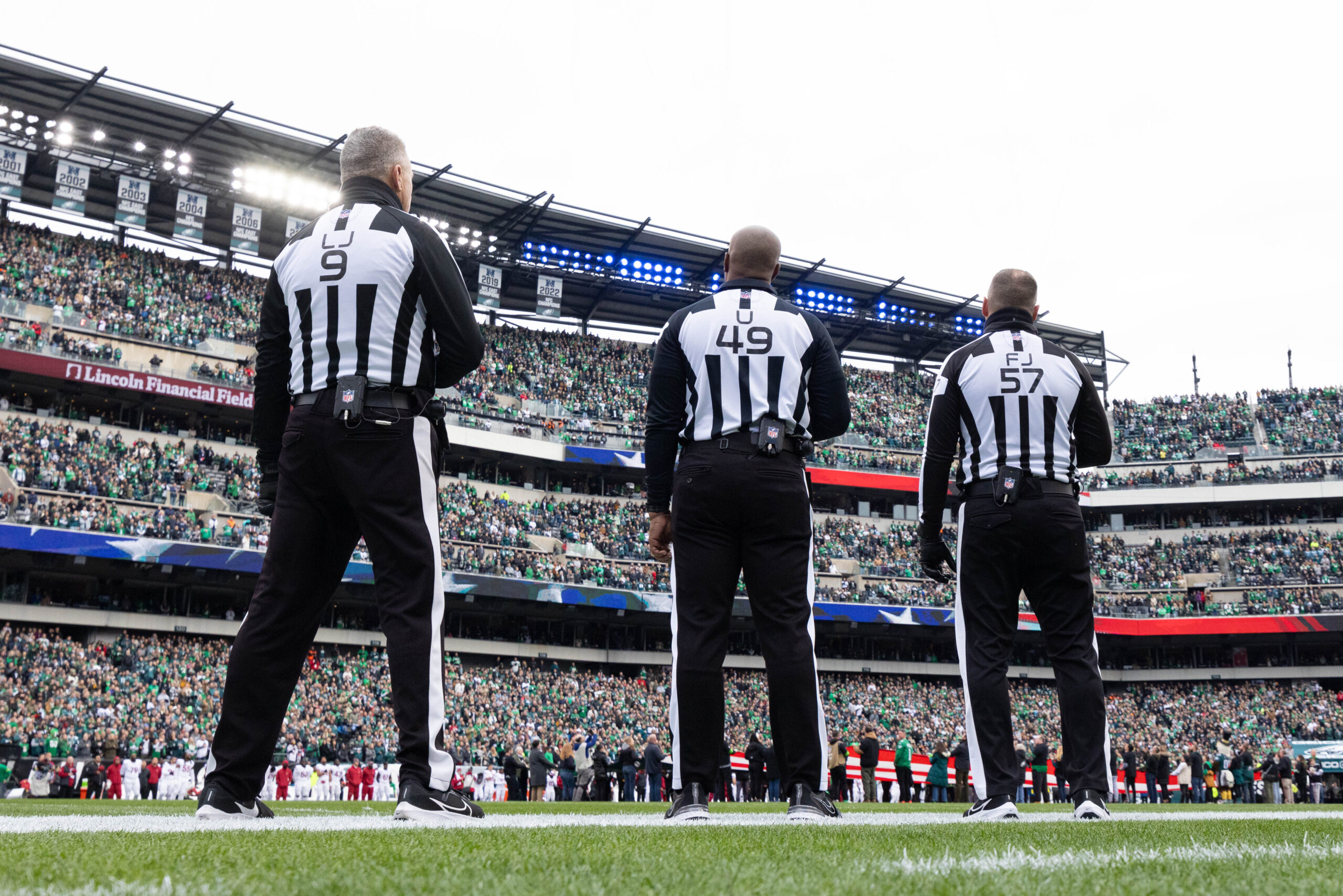 Three officials stand on the field during the National Anthem.