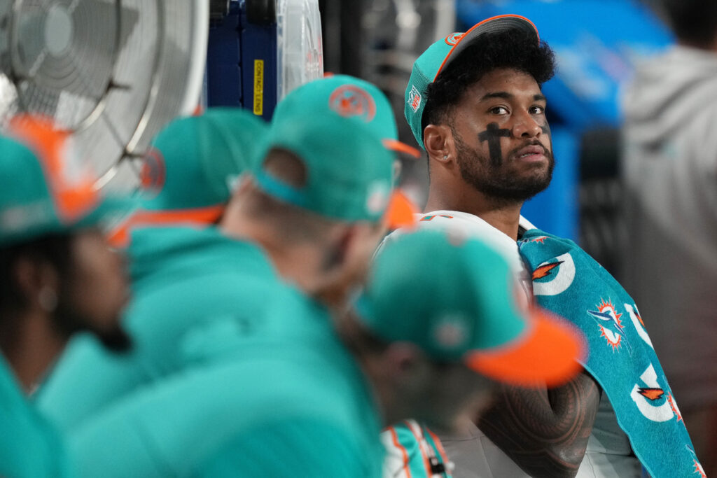 Tua sits on the bench with his helmet off; he's in focus while the rest of the players aren't