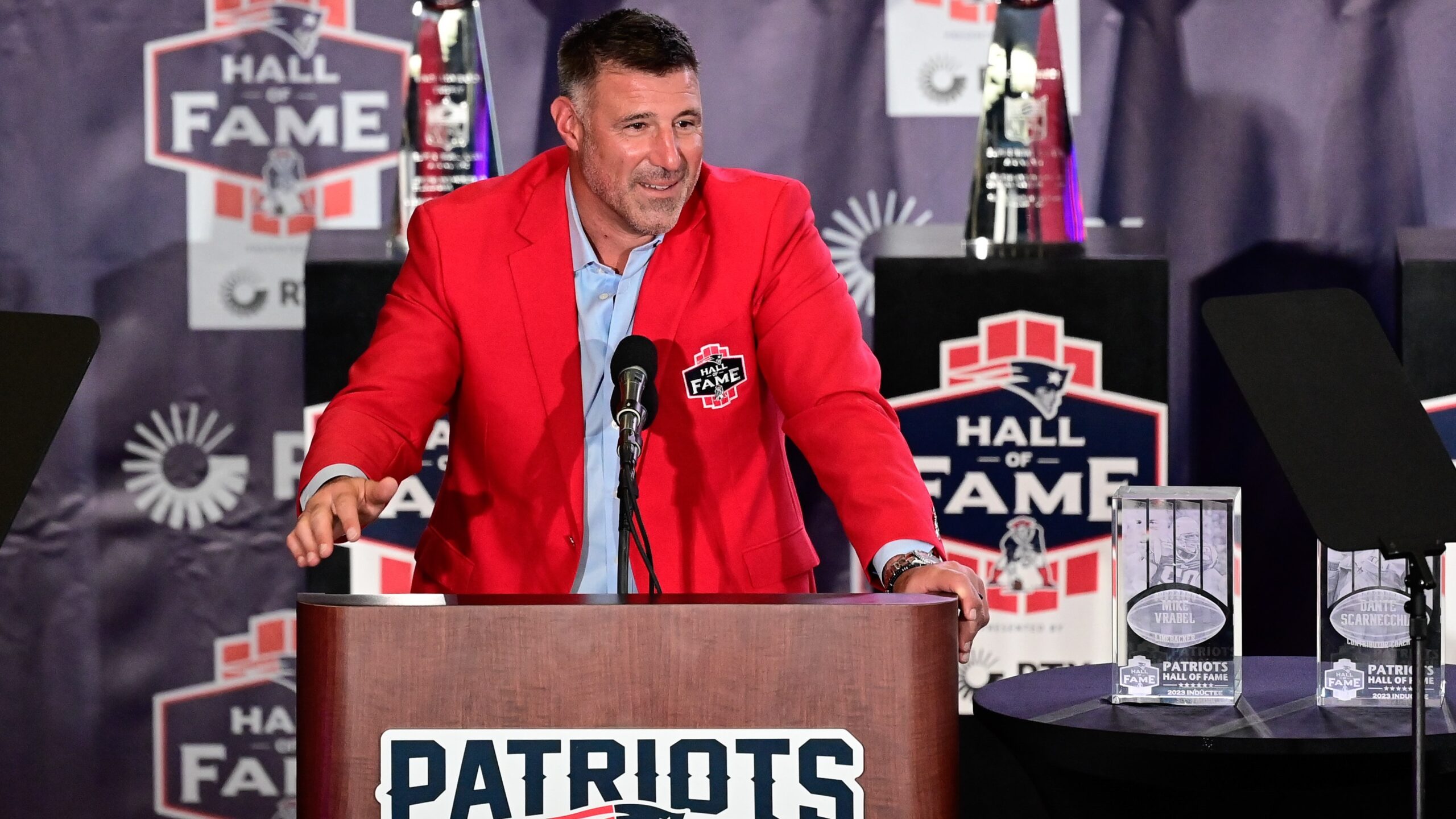 Mike Vrabel at a Patriots podium in a red jacket