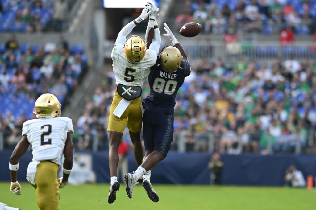 Cam Hart and a Navy player both go up for a pass; the ball sails to the right as the two have their hands intertwined