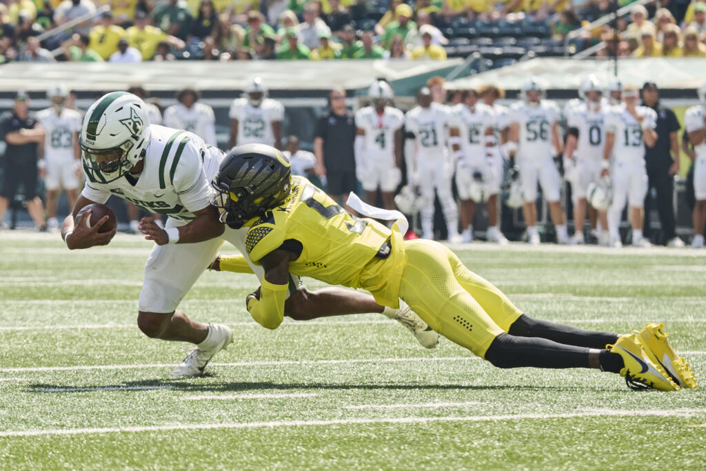 Khyree Jackson, in a neon uniform and black helmet, stretches his body out to make a tackle