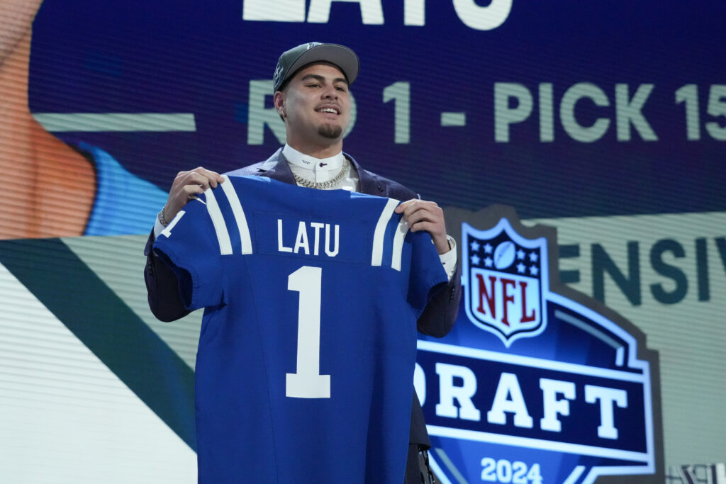 Upper-body image of Indianapolis Colts edge rusher Laiatu Latu holding up a blue Colts jersey with his last name on it on the stage of the NFL Draft