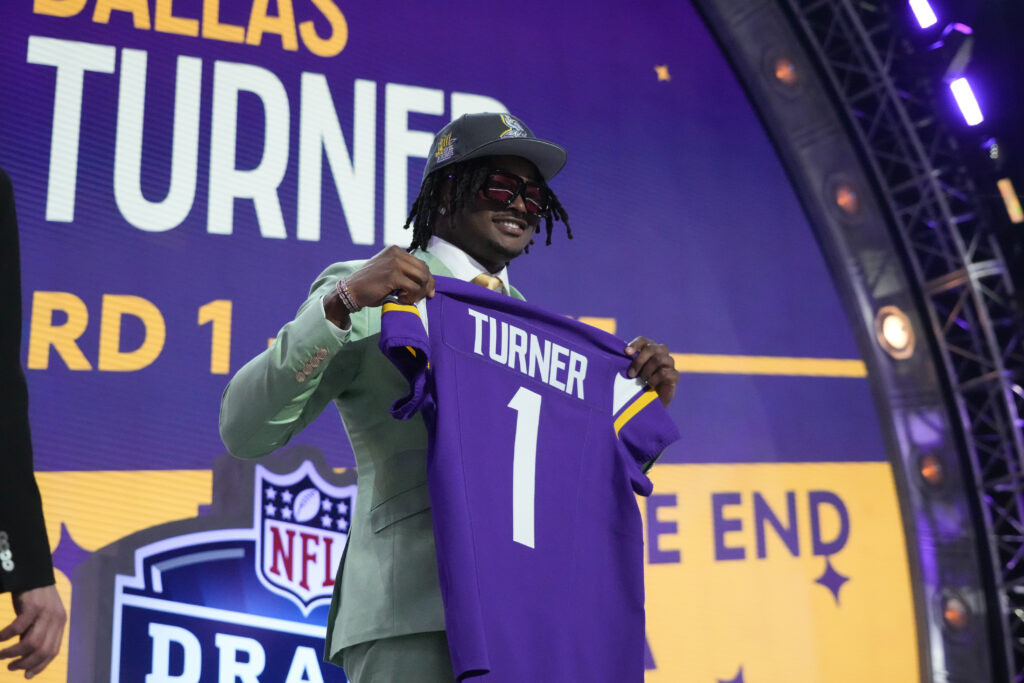 Dallas Turner, in a suit, holds up a Minnesota Vikings jersey with his last name on it on the stage of the draft