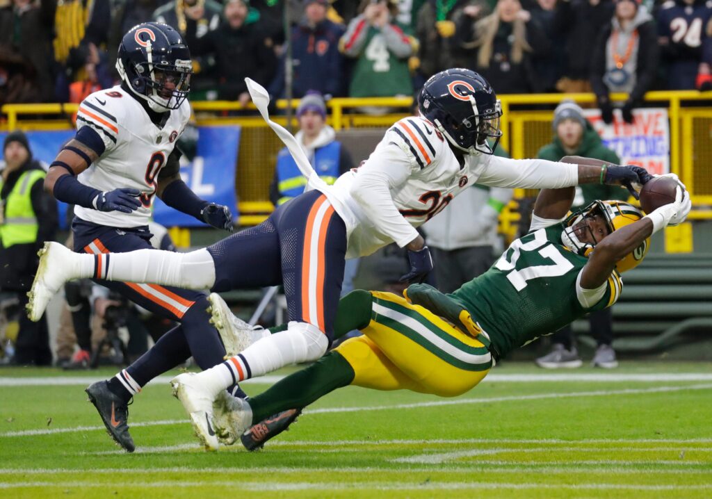 Chicago Bears CB Tyrique Stevenson (white jersey, navy pants and helmet with orange accents) lays out with his left arm extended to get a hand on the ball in the hands of a wide receiver