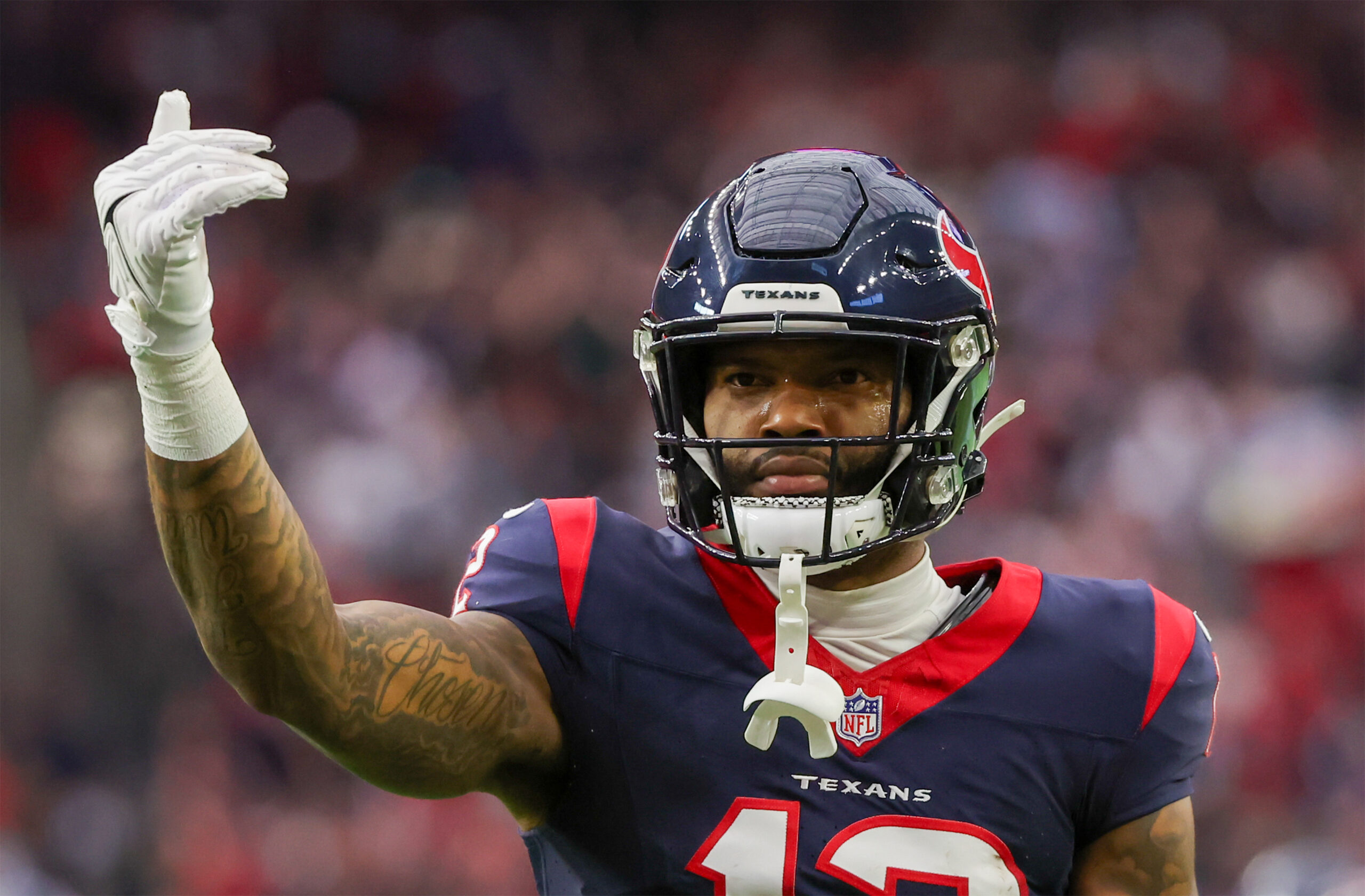 upper-body image of Houston Texans WR Nico Collins (navy jersey and helmet with red accents) as he holds up his right arm in celebration