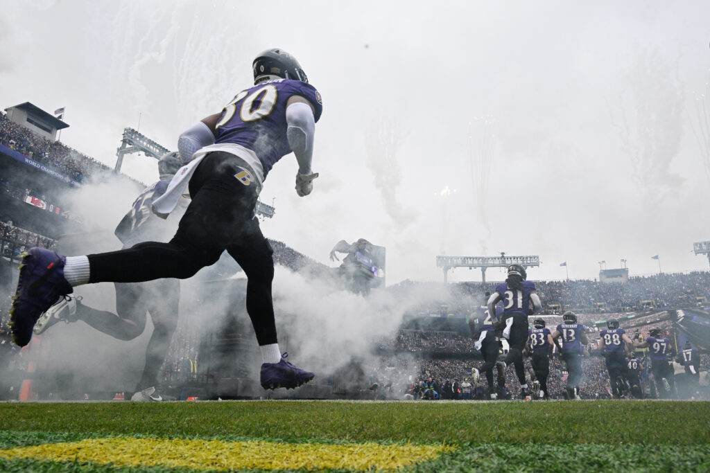 An image from down low of Baltimore Ravens linebacker Trenton Simpson (purple jersey, black pants) running onto the field in a cloud of smoke
