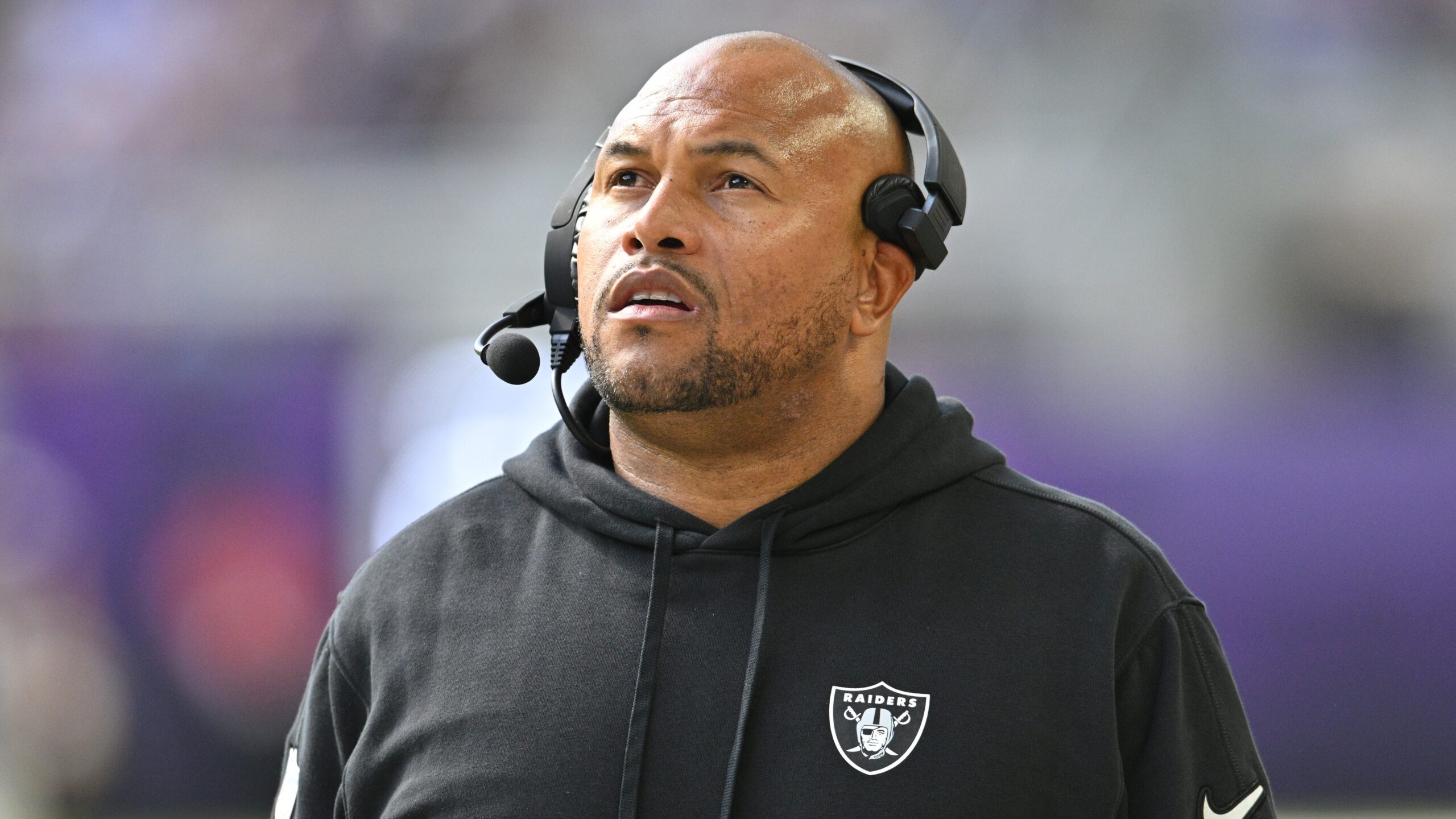 Antonio Pierce stands looking upwards with his headset on and a blurry backdrop.