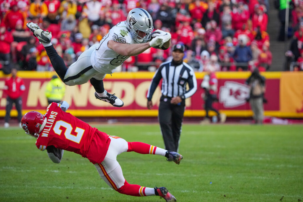 Las Vegas Raiders tight end Brock Bowers (89) leaps with the ball as Kansas City Chiefs cornerback Joshua Williams (2) defends during the first half at GEHA Field at Arrowhead Stadium.