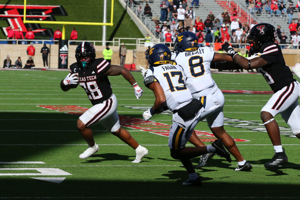 Texas Tech Red Raiders running back Tahj Brooks (28) runs the ball against West Virginia Mountaineers defensive back Dontez Fagan (13) and defensive back Tyrin Bradley Jr. (8) at Jones AT&T Stadium and Cody Campbell Field.