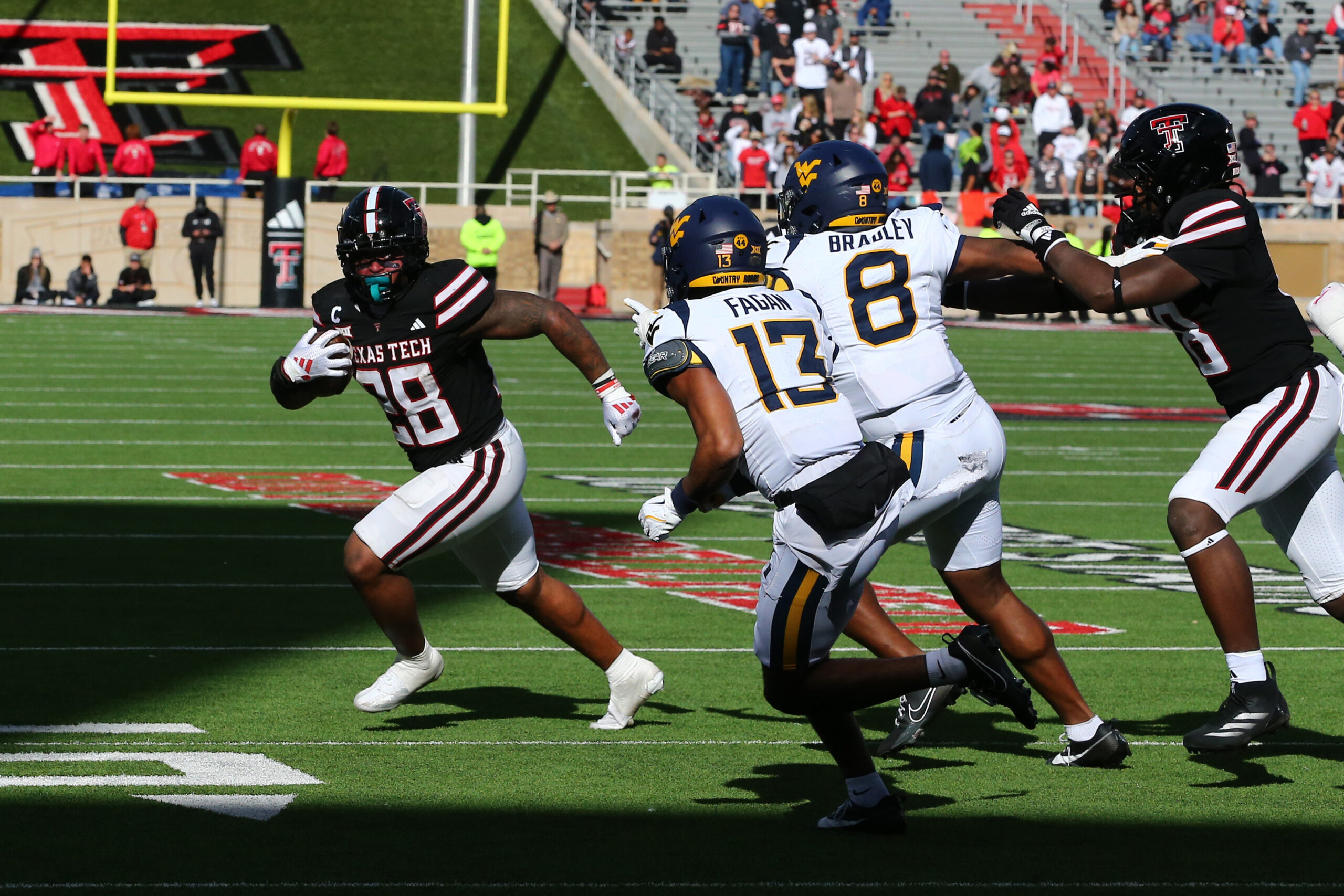 Texas Tech Red Raiders running back Tahj Brooks (28) runs the ball against West Virginia Mountaineers defensive back Dontez Fagan (13) and defensive back Tyrin Bradley Jr. (8) at Jones AT&T Stadium and Cody Campbell Field.